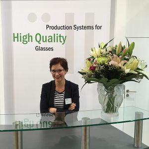 Alexandra Füller standing in front of a wall with the lettering " Production Systems for High Quality Glasses"